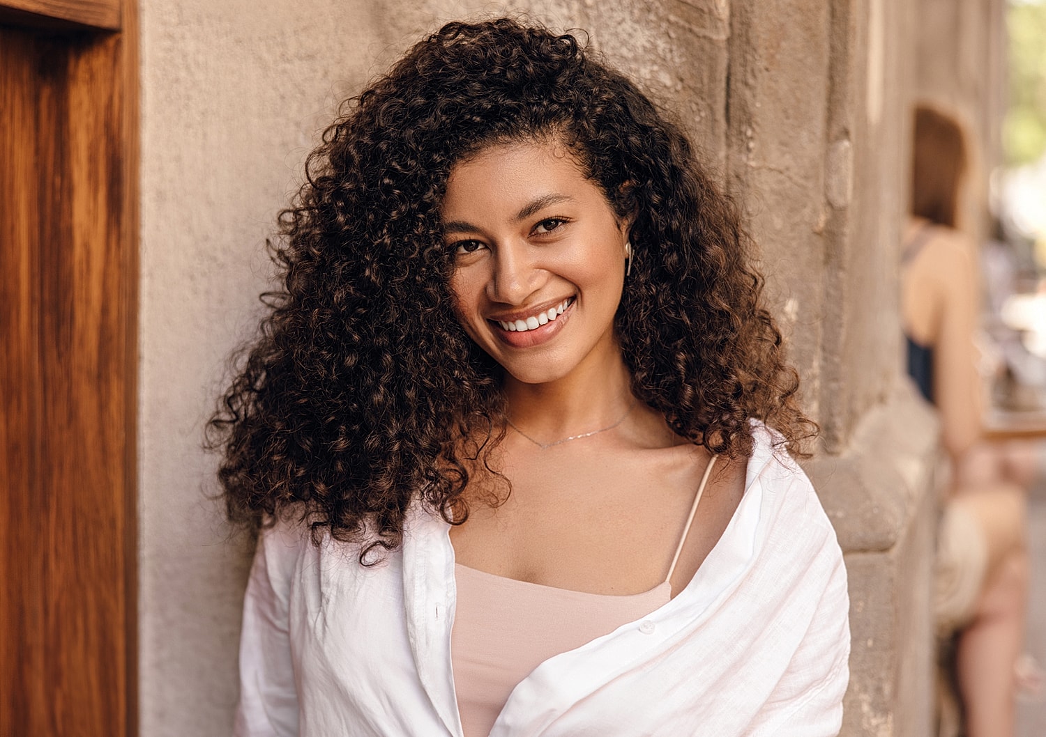 Beverly Hills plastic surgery model with curly hair against a wall.